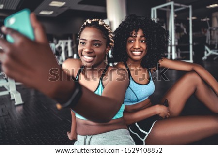 Two attractive sportive afro women in the gym do selfie. Friends on training
