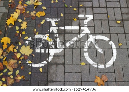 A bike sign on the sidewalk is strewn with autumn yellow maple leaves. The end of the bike season. Autumn in the city.