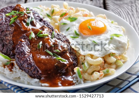 loco moco of white rice, topped with a hamburger patty, a fried egg, brown gravy, and macaroni salad served on a white plate on a rustic wooden table, Hawaiian cuisine, view from above,  Royalty-Free Stock Photo #1529427713