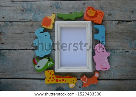 Artistic mockup for your artwork with wooden animal toys and empty card in a white frame shot from the top. Flat lay arrangement with space for text. Happy childhood.