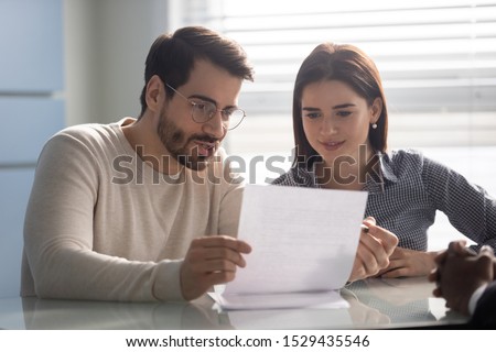 Young husband discussing contract details with smiling wife. Married couple reading carefully terms of conditions of paper document, making decision about house purchase or financial investment.
