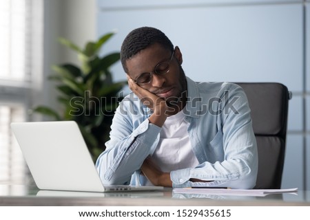 Exhausted young african american employee worker in eyeglasses put head on hand, sleeping at workplace. Head shot tired mixed race entrepreneur manager businessman daydreaming, relaxing at office. Royalty-Free Stock Photo #1529435615