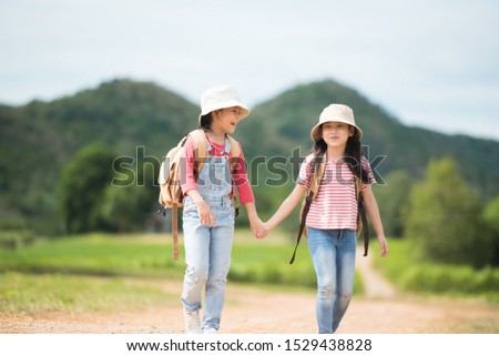 Two children carrying a backpack in the back and wearing a hat for a walk on a country road. She walked and enjoyed the surrounding nature. She enjoys traveling during the summer.