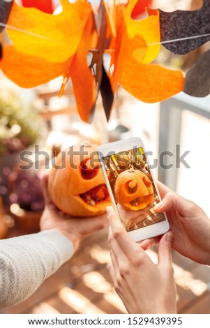Young couple man and woman taking photo of jack-o'-lantern on smartphone preparing for halloween close-up