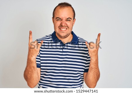 Young man wearing casual striped polo standing over isolated white background shouting with crazy expression doing rock symbol with hands up. Music star. Heavy music concept.