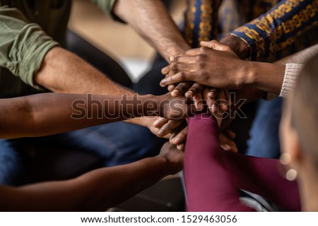 Cropped close of diverse businesspeople putting their hands on top of each other wearing casual clothes and african patterns. Royalty-Free Stock Photo #1529463056