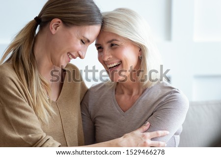 Close up view different generations beautiful women, aged mother and adult daughter touch foreheads laughing embracing sitting close to each other on couch, unconditional love, relative people concept Royalty-Free Stock Photo #1529466278