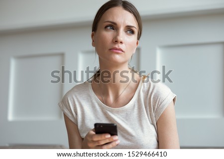 Pensive thoughtful young 30s woman holding smartphone look away lost on sad thoughts waiting first step from man, call or text message or date invitation from boyfriend feels jealousy and concerned Royalty-Free Stock Photo #1529466410