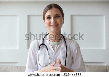 Head shot of woman wearing white coat stethoscope on shoulders looking at camera, doctor make video call interact through internet talk with patient provide help online counseling and therapy concept Royalty-Free Stock Photo #1529466836