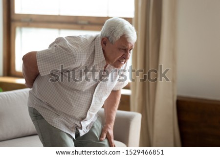 Senior grey haired 70s years man got up from couch writhes in pain felt sharp ache suffers from low back strain, touch loin reduce backache. Degenerative disk disease, pinched nerve rheumatism concept Royalty-Free Stock Photo #1529466851