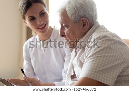 Senior man patient and young woman caregiver medical worker in uniform hold clipboard noting personal information talking listens client telling about health complaints, care support nursing concept Royalty-Free Stock Photo #1529466872