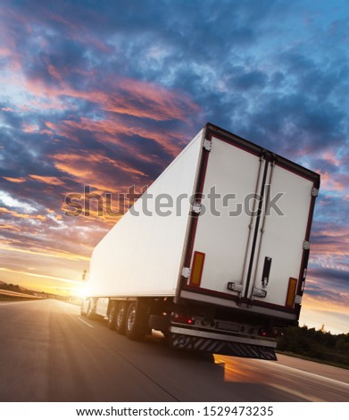 Backview of european truck vehicle on motorway with dramatic sunset light. Cargo transportation and supply theme.