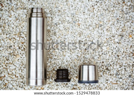 Stainless steel thermos for hot drinks, isolated on white stones.