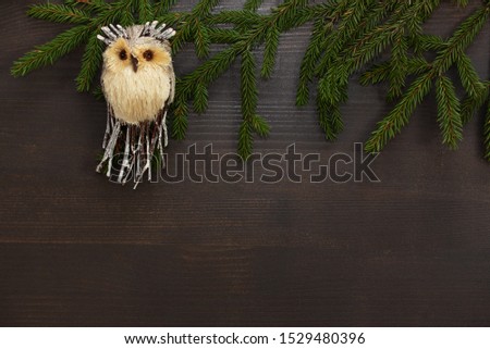Christmas background. A toy owl with green fir branches on a wooden brown background. Christmas toy.Frame for Christmas text. Top view. Copy space.