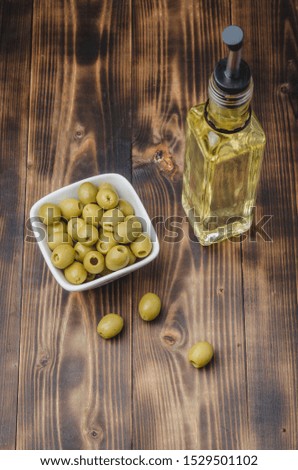 Glass bottle of olive oil and olive in a white bowl on a wooden background. Top view. Organic olive oil concept