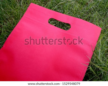 Red ECO bag of non woven fabric, flat lay on a green background, top view