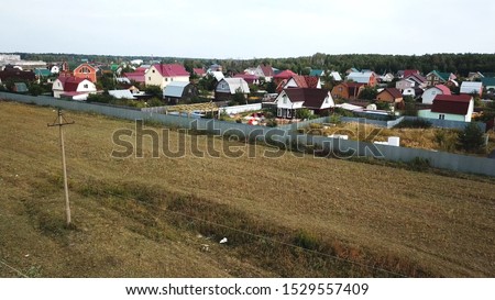 Aerial view of cottage village near the empty field for future building in the end of summer against blue cloudy sky. Stock footage. Beautiful countryside landscape