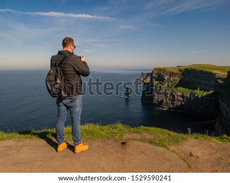 Male tourist taking picture of Cliff of Moher on his smart phone, Sunny warm day., Concept capturing and sharing memory through the modern technology, travel.