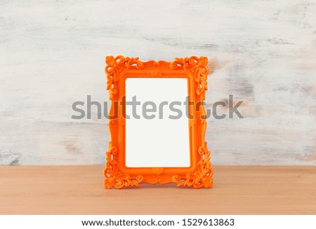 blank orange photo frame over wooden table and white background. Ready for photography montage