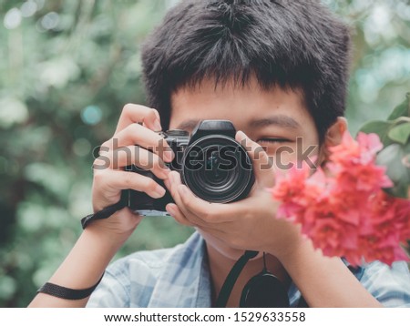 Young asian boy looking for attractive and taking photo by camera on forest background and nature holiday. Travel concept