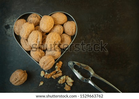 Bunch of walnut shells in metallic heart cookie cutter a metallic nutcracker and nut kernels on dark grunge metallic background closeup from above with copy space    