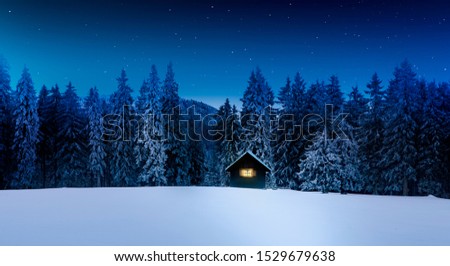 Log cabin with shining window in wintry forest