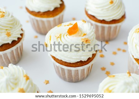 Group of homemade cupcakses with cream, orange candied fruit and gold confectionery sprinkling at white table background. Main cupcake in the center. Picture for a menu or a confectionery catalog.