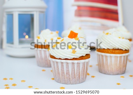Cupcake with cream, orange candied fruit at the top and gold confectionery sprinkling with lantern at blue and red background. Picture for a menu or a confectionery catalog.