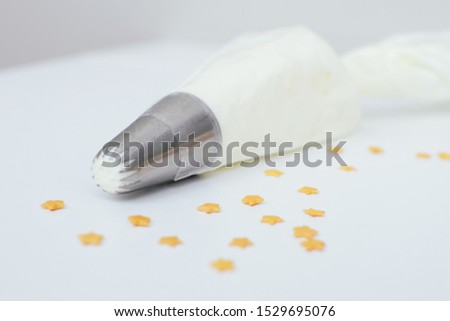 Simple pastry bag with white cream, and gold confectionery sprinkling pictured at the home's kitchen table. Picture for a menu or a confectionery catalog.
