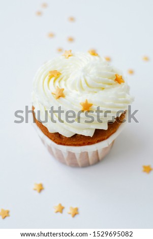 One cupcake with cream, at the top and gold confectionery sprinkling with lantern at background. Picture for a menu or a confectionery catalog.