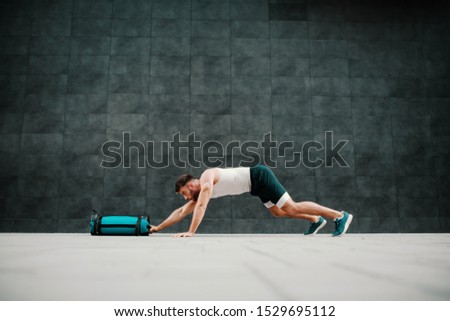 Side view of handsome fit muscular caucasian man doing inchworms with training bag. Royalty-Free Stock Photo #1529695112