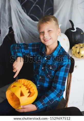Young white boy cutting scary face in pumpkin for Halloween celebration. Vertical color photo.