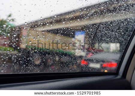 Raindrops on window glass of the car with blurry light from outside highway street background.