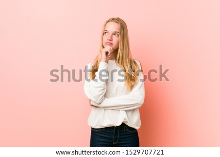 Young blonde teenager woman looking sideways with doubtful and skeptical expression.