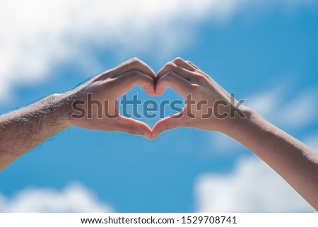The hands of women and men in the form of hearts with blue skies and clouds Hands in the form of love hearts - love concepts