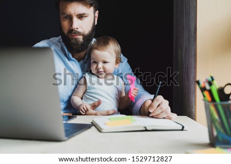 Parent with child studying remotely at homebased laptop. Distant education for people with babies. Young man and toddler sitting in front of laptop. Father with infant watching video lessons, webinars Royalty-Free Stock Photo #1529712827
