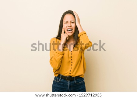 Young hispanic woman against a beige background whining and crying disconsolately.