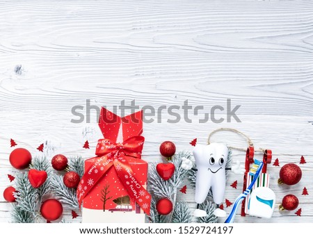 Dentist Merry Christmas New Year Concept cute cartoon tooth with toothbrush and dental floss on white wooden xmas background with decorations and gift box. Top view, flat lay. 