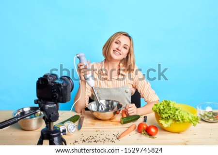 Joyful attractive housewife broadcasting video for her personal account in social network, making delicious vegetarian meal by new recipe, telling culinary hacks, smiling friendly at camera.