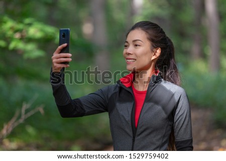 Phone active woman taking picture with mobile cellphone outside on forest nature walk during cardio activity holding smartphone.