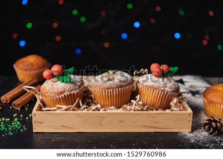 Christmas cupcakes decorated with mistletoe in a wooden box. Multi-colored bokeh in the background. Christmas sweet food. Mini muffins.