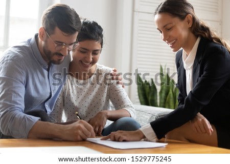 Happy married diverse couple signing contract, making legal deal, taking loan or mortgage, purchasing real estate, new apartment, husband in glasses embracing wife, putting signature on documents