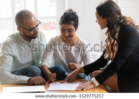 Happy diverse couple satisfied clients making deal, Indian wife signing contract at meeting after successful negotiation with realtor, mortgage insurance broker, family purchasing new apartment Royalty-Free Stock Photo #1529775257