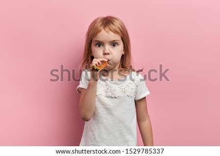 funny pleasant little kid using blowing horn, celebrating birthday, having a party, close up portrait, isolated pink background, studio shot, childhood