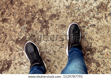 Female legs in black stylish fashionable sneakers and blue jeans. View from above. Concrete walkway with stones. Walk in the park