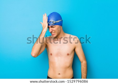 Young swimmer man forgetting something, slapping forehead with palm and closing eyes.