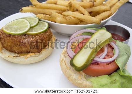 Crabcake Burger Open Face with Pickle Onion Tomato Lettuce Lemon Slices and French Fries Closeup