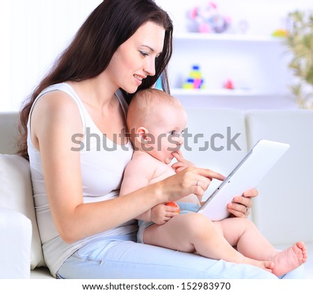 mother and baby are looking to play and read tablet computer on the couch at home