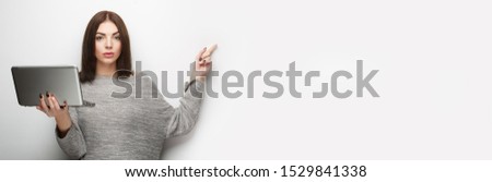 Mockup. Woman with laptop on light gray background pointing finger to an empty space ready for custom text. Copyspace. Banner format.