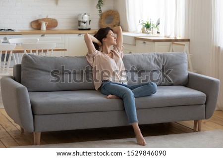 Calm serene young woman relaxing on comfortable couch at home with closed eyes and hands behind head, satisfied girl stretching on sofa, daydreaming and meditating in cozy living room Royalty-Free Stock Photo #1529846090